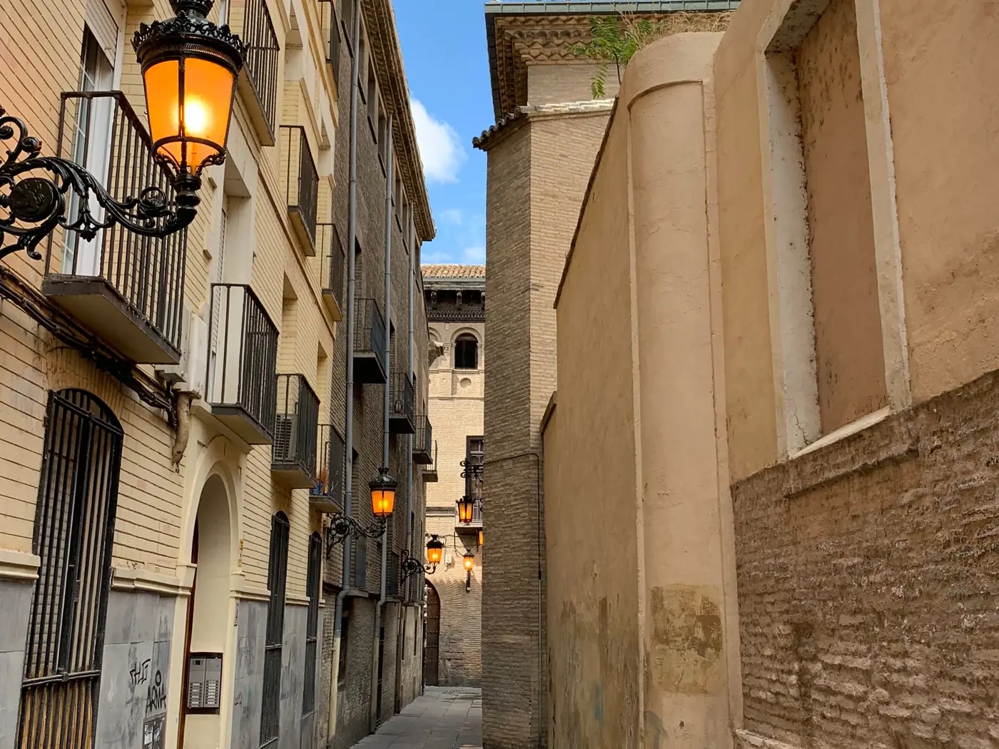 Calle estrecha de casco antiguo español, con faroles de forja encendidos y fachadas de ladrillo